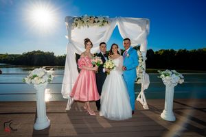 Lakeside wedding ceremony setup with white draped arch and columns during golden hour.