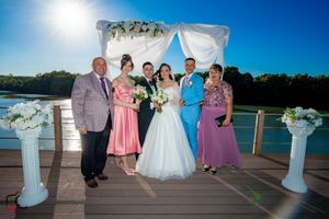 Wedding party gathered on deck with water view and decorative white columns.
