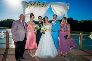 Formal wedding group portrait on waterfront deck with floral arch and columns.