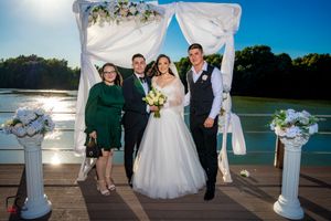Waterfront wedding ceremony setup with white draped arch and floral decorations on wooden deck.