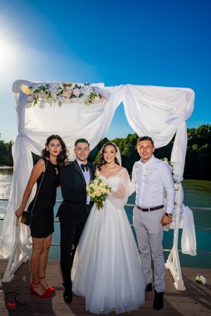 Casual wedding group photos taken on deck with white fabric arch and water views.