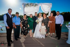 Large wedding group photo session on deck with decorated arch and lake backdrop.