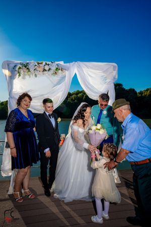 Family members gather for photos under a white wedding arch on a lakeside deck.