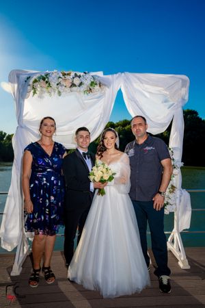 Wedding celebration photos with guests on waterfront deck featuring white fabric backdrop.