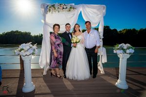 Outdoor wedding photography session on wooden pier with decorative white arch and flowers.