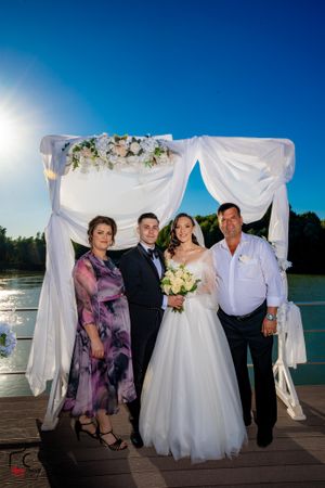 Wedding party poses for formal photos on dock with white fabric arch and lake view.