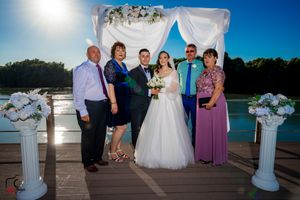 Lakeside wedding ceremony setup with white columns and fabric arch for family photos.
