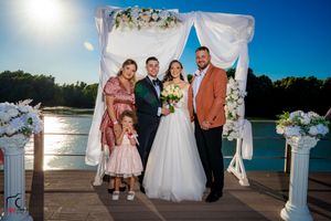 Wedding party group shots on dock with floral arch and water backdrop at sunset.