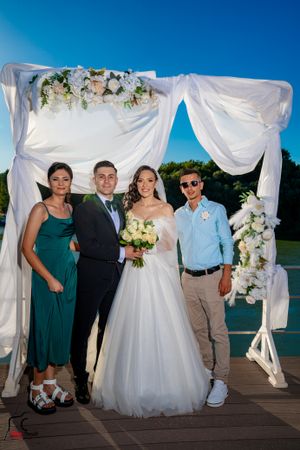 Outdoor wedding photos with decorated arch and waterfront view on wooden deck.