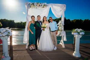 Wedding celebration portraits on lakeside deck with white draped arch and flowers.