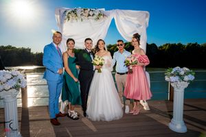 Wedding ceremony setup on a lakeside dock with white fabric draped archway and floral decorations at sunset.
