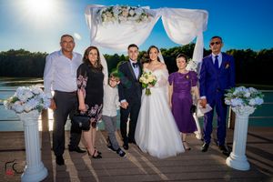 Wedding celebration group photos on wooden dock with lake and trees in background at dusk.