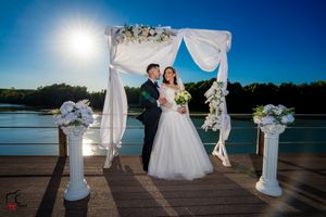 Lakefront wedding setup with flowing white fabric and floral arrangements against bright blue sky.