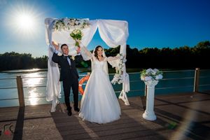 Wedding celebration on waterfront dock with decorative white arch and sunlit lake backdrop.
