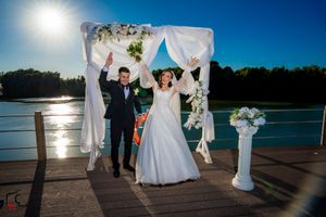 Romantic waterfront wedding ceremony setup with white drapes and chairs against a stunning sunset backdrop.