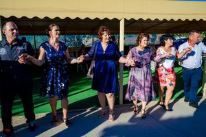 Panoramic view of wedding guests participating in a line dance outdoors.