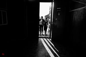 Silhouettes of figures stand in a doorway casting dramatic shadows across a dark interior floor.