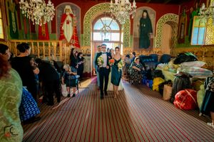 Wedding guests gather inside an ornate orthodox church with religious icons and chandeliers.