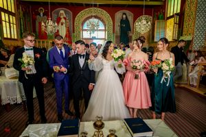 Wedding party poses for photos inside an ornate orthodox church with religious artwork and chandeliers.