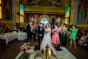 Wedding ceremony in progress inside ornate orthodox church with religious artwork and chandeliers.