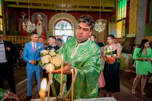 Orthodox priest in green vestments performs ceremony in decorated church interior.