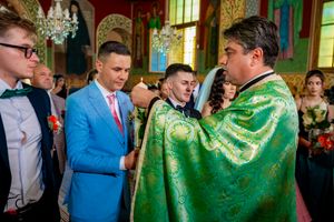 Orthodox priest in green robes performs religious ceremony with attendees in formal attire.