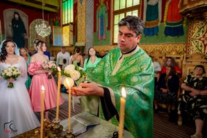 Orthodox priest conducts wedding ceremony while holding ceremonial items in decorated church.