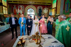 Wedding guests gather in a colorful Orthodox church interior with decorative patterns and stained glass windows.