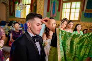 Religious ceremony taking place in an ornately decorated Orthodox church with golden details and green vestments.