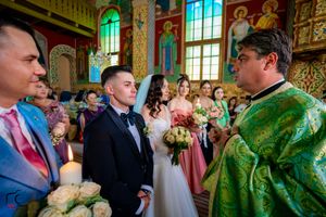 Wedding party stands in ornate Orthodox church with vibrant green and gold decor during ceremony.