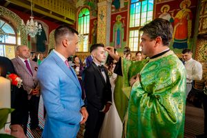 Orthodox wedding ceremony participants gather in richly decorated church with golden icons and green vestments.