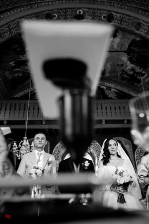 Black and white wedding scene photographed through architectural details in an ornate venue.