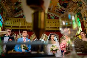 Blurred foreground frames a wedding ceremony in an elaborately decorated historic venue.