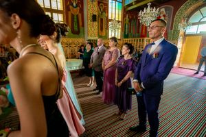 Guests gather in an ornate church hall with decorative murals and a striped carpet for a wedding ceremony.