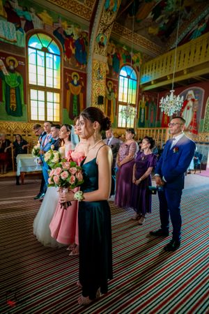 Wedding attendees line up in formal attire inside a grand church hall with painted walls and patterned floors.