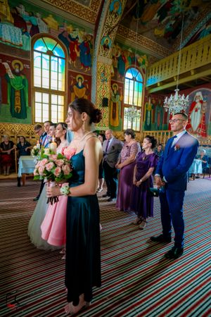 Wedding party members stand in formation inside an elaborately decorated church with striped flooring.