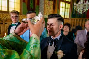 Traditional wedding crowns are held during an Orthodox ceremony in a decorated church setting.