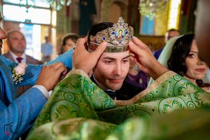 Traditional wedding crowns are held during Orthodox ceremony with green and gold decor.