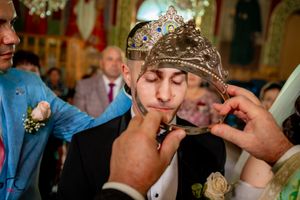 Close-up of wedding ceremony with ornate crown and veil against decorated church background.