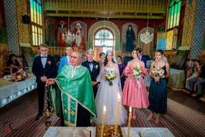 Wide shot of a wedding ceremony in a decorated church interior with stained glass windows.