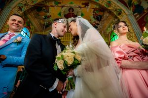 Wedding celebration in an ornate Orthodox church with painted ceiling and traditional decorations.