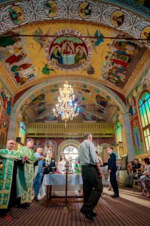 Ornate church hall with painted ceiling murals and crystal chandeliers during wedding ceremony.