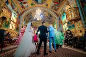 Panoramic view of wedding ceremony in decorated hall with painted ceiling and stained glass windows.
