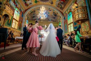 Wedding celebration in an ornate ballroom with elegant chandeliers and decorative ceiling artwork.