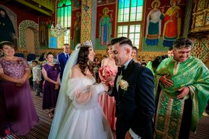 Orthodox wedding ceremony being performed in a church with vibrant stained glass and painted murals.