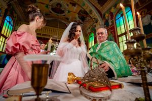 Orthodox wedding ceremony with attendants in pink and green vestments at decorated altar.
