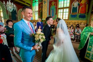 Wedding celebration inside an elaborate orthodox church with green-lit stained glass windows.