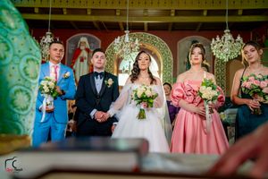 Wedding party standing in front of ornate church altar with gold accents and chandeliers.