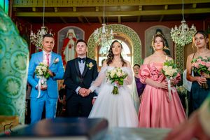 Wedding party poses in front of ornate gold archway and religious icons during ceremony.