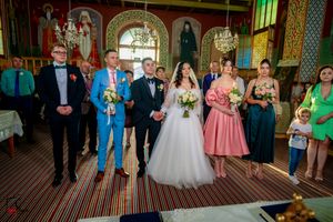Wedding party lined up in an Orthodox church with vibrant stained glass and decorative walls.